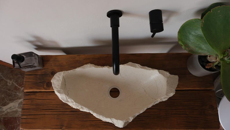 Hand-carved Crema Marfil marble sink with glossy inner bowl and raw edge, installed on rustic wood vanity.