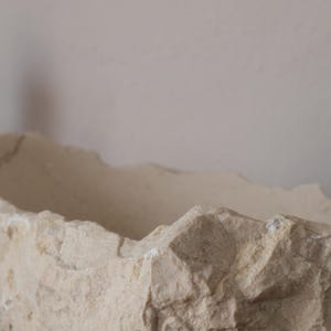 Close-up of raw chiseled marble edge showing the natural beige texture of Crema Marfil stone.