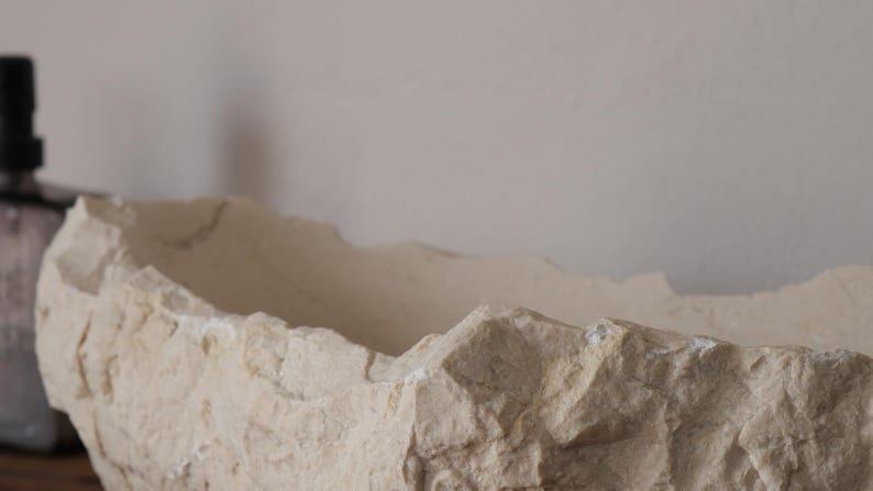 Close-up of raw chiseled marble edge showing the natural beige texture of Crema Marfil stone.