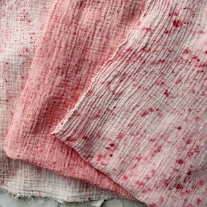 Puede incluir: Tres piezas de tela rosa y blanca con un patr&oacute;n moteado. La tela est&aacute; doblada y superpuesta, mostrando diferentes tonos de rosa.
