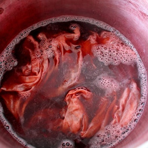 Puede incluir: Primer plano de una olla llena de l&iacute;quido rojo y tela. La tela est&aacute; sumergida en el l&iacute;quido y parece estar empap&aacute;ndose en el tinte rojo.