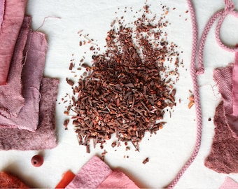 May include: A pile of dried red dye chips on a white surface, surrounded by fabric swatches in various shades of pink and red.