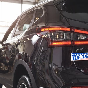 May include: A black SUV with a red, white, and blue "REAGAN" bumper sticker.