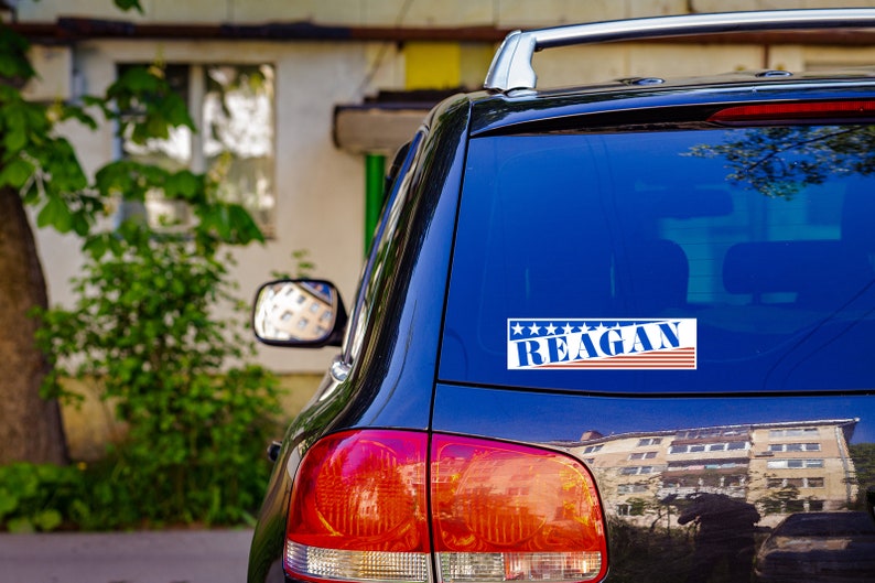 May include: A black car with a blue and red sticker on the back window that says "Reagan" with stars above the text.