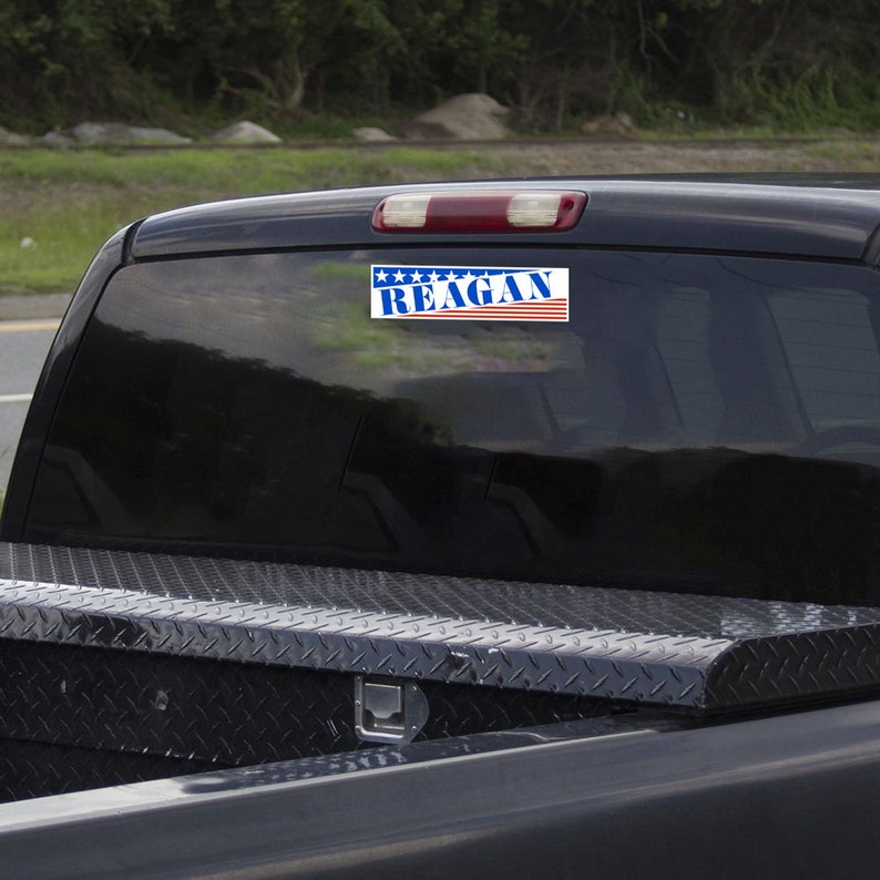 May include: A black pickup truck with a sticker on the back window that says "REAGAN" with a red, white, and blue American flag design.