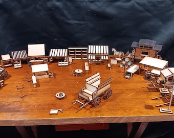 May include: A collection of wooden miniature buildings, wagons, and other structures, all crafted from laser-cut wood. The pieces are arranged on a wooden table, creating a miniature town or village scene.