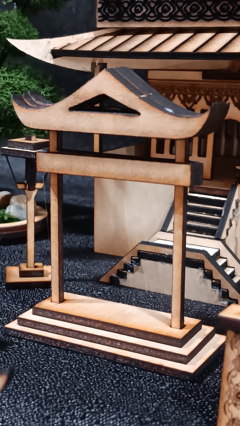 May include: A wooden model of a traditional Japanese gate, or torii, with a curved roof and two pillars. The gate is made of light brown wood and has a dark brown base.