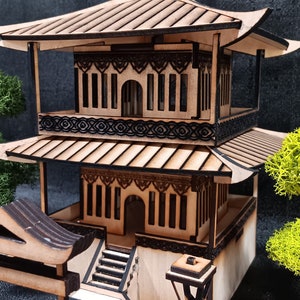 May include: A wooden model of a traditional Asian pagoda with a tiered roof, intricate details, and a small lantern. The model is set on a wooden base and includes a small gate and steps.