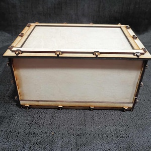 May include: A wooden box with a light brown finish and a dark brown trim. The box has a hinged lid and a simple design.