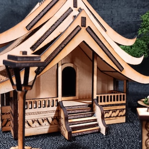 May include: A wooden model of a traditional Asian house with a curved roof and intricate details. The house has a small porch and a lamppost in front. The model is made of light brown wood and has a natural finish.