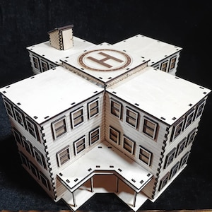 Puede incluir: Un modelo de madera cortado con láser de un edificio de varios pisos con una plataforma para helicópteros en el techo. El edificio tiene múltiples ventanas y un pequeño edificio auxiliar. El modelo está hecho de madera clara con detalles en marrón oscuro.