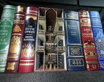May include: A bookshelf with a miniature library inside. The bookshelf is made of wood and has a dark brown finish. The miniature library has a wooden floor and a white ceiling. There are bookshelves on all four walls, and there are books on the shelves. There are also a few chairs and a table in the miniature library.