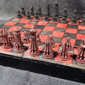 Könnte beinhalten: Ein Schachspiel aus Holz mit roten und schwarzen Figuren. Das Brett ist aus dunklem Holz mit einem rot-schwarzen Schachbrettmuster. Die Figuren sind aus dunklem Holz mit einer roten Oberfläche. Das Set ist in geschlossener Position, wobei die Figuren in ihren Startpositionen angeordnet sind.