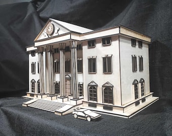 May include: A white, wooden model of a building with black trim and a clock on the front. The building has a large, white, wooden porch with black columns. A small, silver car is parked in front of the building.