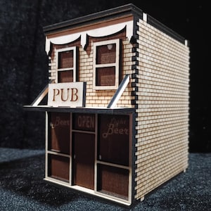 May include: A miniature wooden pub model with a detailed exterior. The building features a sign that reads "PUB" and "OPEN", with "Beer" and "Light Beer" signs. The walls are made of small wooden shingles, and the windows are visible.