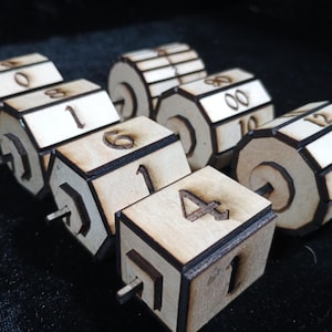 May include: A collection of wooden dice with numbers etched on the sides. The dice are light brown with dark brown edges and feature numbers from 0 to 12. Each die has a wooden dowel extending from the center.