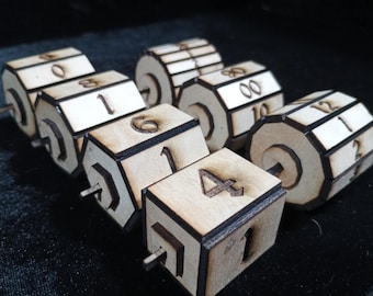 Puede incluir: Un conjunto de dados de madera con números grabados del 0 al 12. Los dados son de color marrón claro con bordes oscuros y tienen un pasador de madera en el centro. Perfectos para juegos.