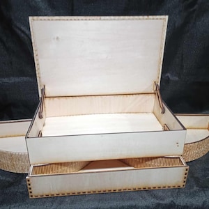 Könnte beinhalten: Eine Holzkiste mit einem Scharnierdeckel und einer herausziehbaren Schublade. Die Kiste ist aus hellem Holz gefertigt und hat eine natürliche Oberfläche. Der Deckel ist geöffnet und die Schublade ist herausgezogen.