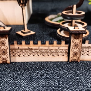 May include: A wooden miniature wall with intricate carvings and two decorative pillars. The wall is made of light brown wood and has a detailed pattern of squares and circles. The pillars are dark brown and have a more ornate design.