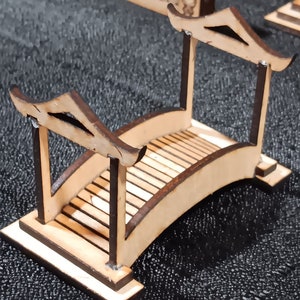 May include: A wooden bridge model with a curved top and a flat base. The bridge is made of light brown wood and has a dark brown stain on the edges. The bridge is about 6 inches long and 3 inches wide.