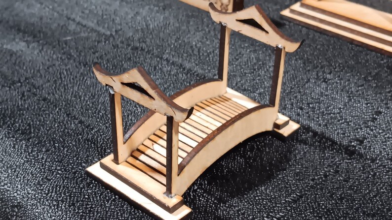 May include: A wooden bridge model with a curved top and a flat base. The bridge is made of light brown wood and has a dark brown stain on the edges. The bridge is about 6 inches long and 3 inches wide.