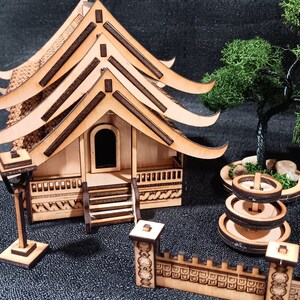 May include: A wooden model of a Japanese temple with a layered roof, a small wooden fence, a fountain, and a tree. The model is made of light brown wood and has intricate details.