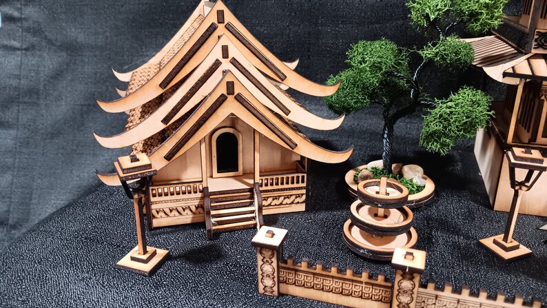 May include: A wooden model of a Japanese temple with a layered roof, a small wooden fence, a fountain, and a tree. The model is made of light brown wood and has intricate details.