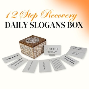 Puede incluir: Una caja de madera con un diseño floral blanco y marrón. La caja contiene tarjetas con citas inspiradoras para la recuperación de 12 pasos. Las tarjetas incluyen frases como "Easy does it", "Principles before personalities", "Feelings are not facts", "Keep it simple", "Just for today", "Progress, not perfection", "Misery is optional", y "Nothing changes if nothing changes".