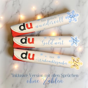 May include: Three white and red candy bars with German text and snowflake designs. The bars have the word "du" in red and black. Each bar has a different phrase: "wundervoll", "Gold wert", and "Weihnachtszauber".