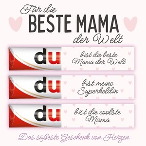 May include: A light pink background with the text "Für die BESTE MAMA der Welt" and three chocolate bars with the word "du" on them. Each bar has a different message: "bist die beste Mama der Welt", "bist meine Superheldin", and "bist die coolste Mama".