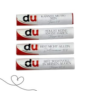 May include: Four chocolate bars with white wrappers and red accents. Each bar has the word "du" printed on it, and a different German phrase with a Bible verse reference. A line drawing of a heart is in the lower left corner.