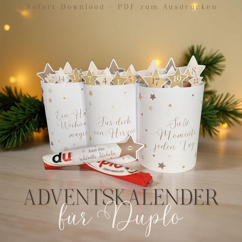 Op de afbeelding: Witte papieren adventskalenderbekers met gouden steraccenten en stervormige toppers met nummers. De bekers hebben Duitse tekst. Een Duplo-reep ligt voor de bekers. De tekst "ADVENTSKALENDER f&uuml;r Duplo" staat onderaan.