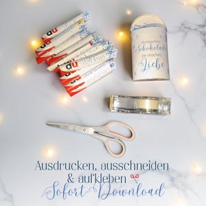 May include: A collection of items including Kinder chocolate bars, a cylindrical container with text, a tape dispenser, and scissors. The chocolate bars have red and white packaging. The container has blue snowflake accents and text. The scissors have pink handles.