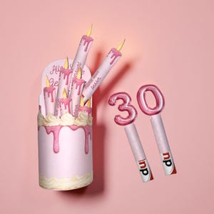 May include: A pink birthday cake-shaped candle holder with several candles and the number "30" candles. The candles have pink wax dripping down the sides. The number "30" candles are pink and white.