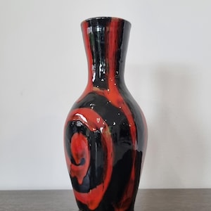 May include: A black and red ceramic vase with a swirling pattern. The vase has a narrow neck and a wide base.