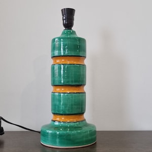 May include: A green and orange ceramic table lamp with a black lampshade. The lamp has a cylindrical base with three bands of orange.