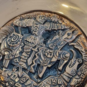 May include: A brass bowl with an intricate design of a knight riding a horse. The design is in a dark blue and gold color scheme.