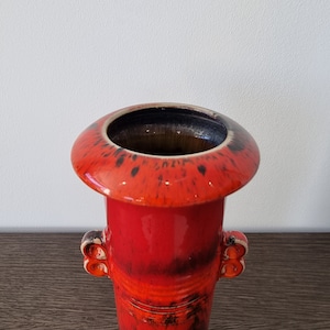 May include: A red ceramic vase with black and orange glaze. The vase has a wide, flared top and two small handles on the sides.