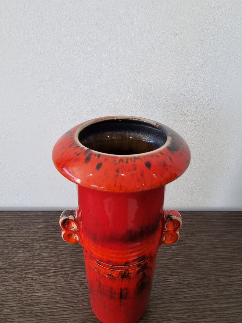 May include: A red ceramic vase with black and orange glaze. The vase has a wide, flared top and two small handles on the sides.