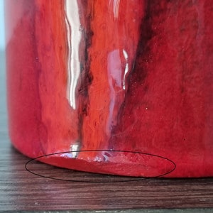 May include: Red ceramic vase with a glossy finish. The vase has a rounded bottom and a slightly uneven edge.