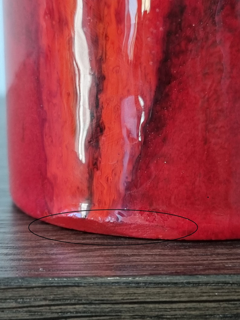 May include: Red ceramic vase with a glossy finish. The vase has a rounded bottom and a slightly uneven edge.