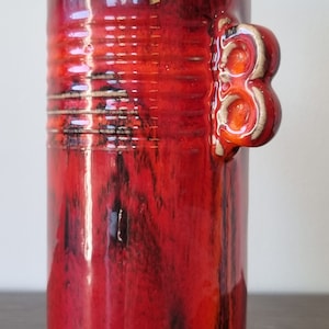 May include: Red ceramic vase with a textured, marbled glaze and a unique three-knob handle.