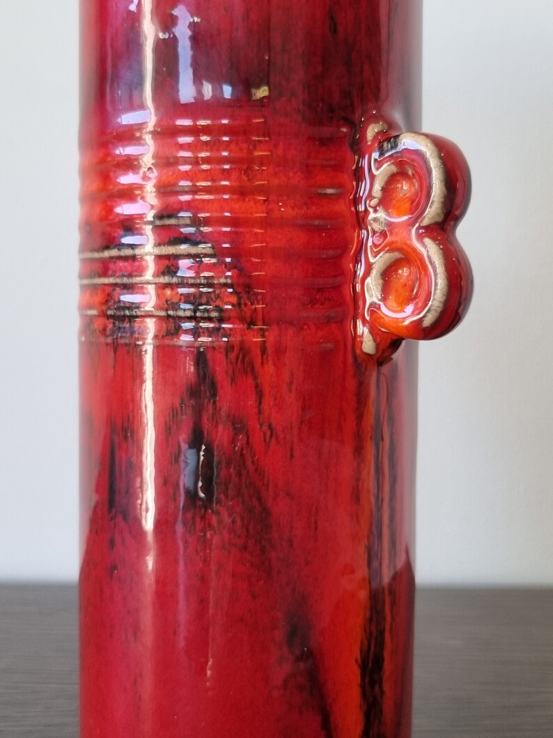 May include: Red ceramic vase with a textured, marbled glaze and a unique three-knob handle.