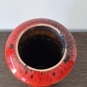 May include: A red ceramic vase with black speckles and a brown glazed interior. The vase has a wide opening and a cylindrical shape.