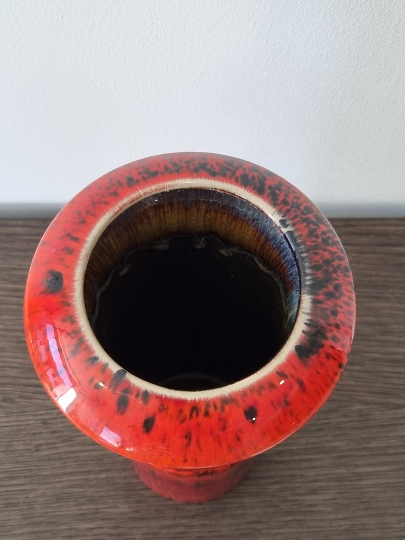 May include: A red ceramic vase with black speckles and a brown glazed interior. The vase has a wide opening and a cylindrical shape.