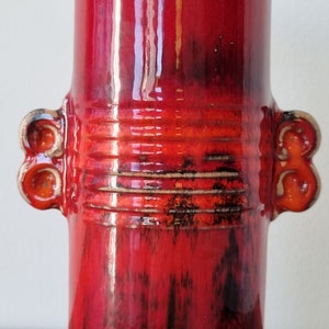 May include: Red ceramic vase with two handles and a textured glaze. The vase has a wide mouth and a narrow base.