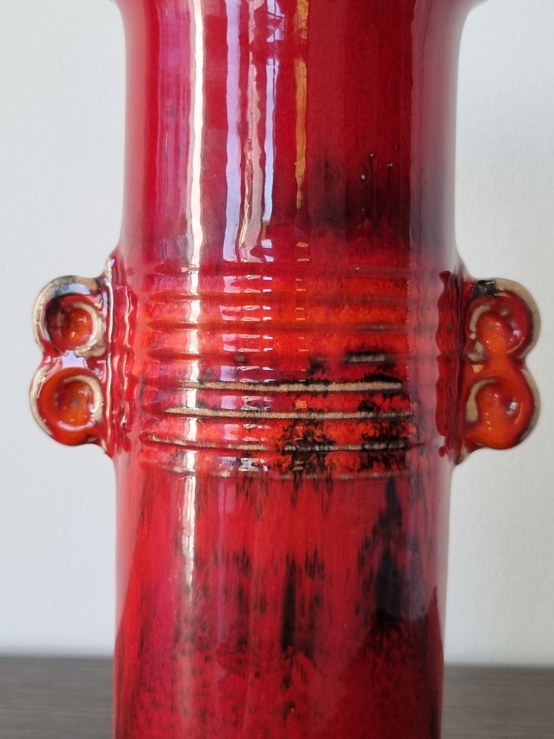 May include: Red ceramic vase with two handles and a textured glaze. The vase has a wide mouth and a narrow base.