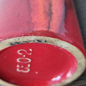 May include: Close-up of the bottom of a red ceramic vase with a white stamp that reads "2.03."