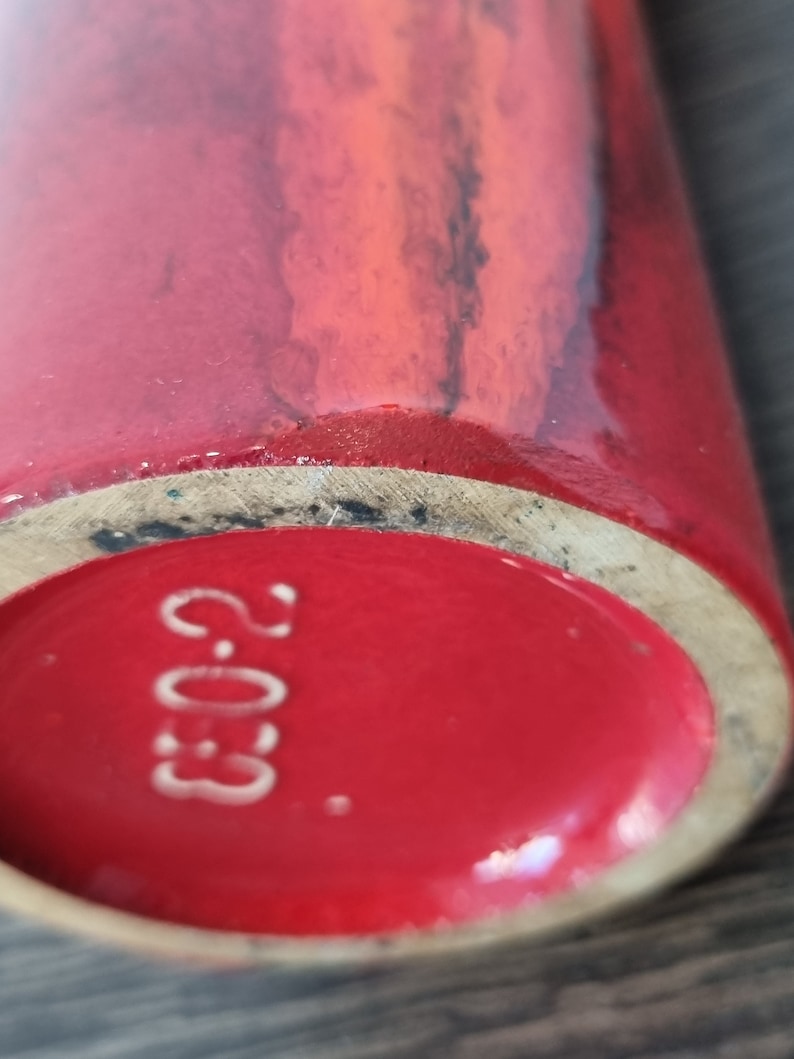 May include: Close-up of the bottom of a red ceramic vase with a white stamp that reads "2.03."