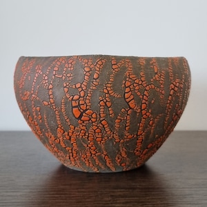 Op de afbeelding: Een keramische kom met een gekrakelde glazuur. De kom is donkerbruin met oranje accenten.